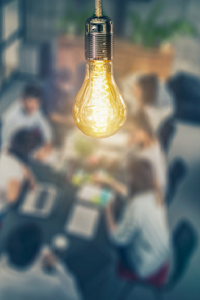 out of focus image of people sat around a table in a business meeting. Bulb shines in the foreground