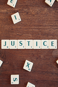 A scrabble board with the word 'JUSTICE' laid out in the centre while random letters are arranged haphazardly.