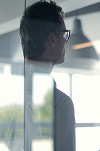 man wearing glasses facing away, viewed through reflective glass