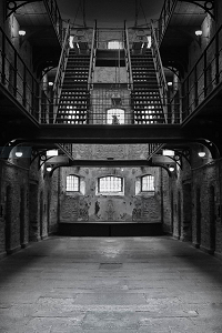 A black and white image depicting the ground floor of a prison atrium including stairs, windows and partial view of cells.