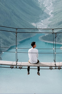 Man sitting on a rope bridge looking out over lake and valley 