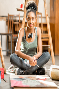 Young lady sat cross legged in a art studio surrounded by art and easels