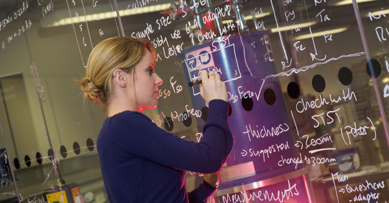Female physicist resolving complex theory on LightBoard (glass wall)