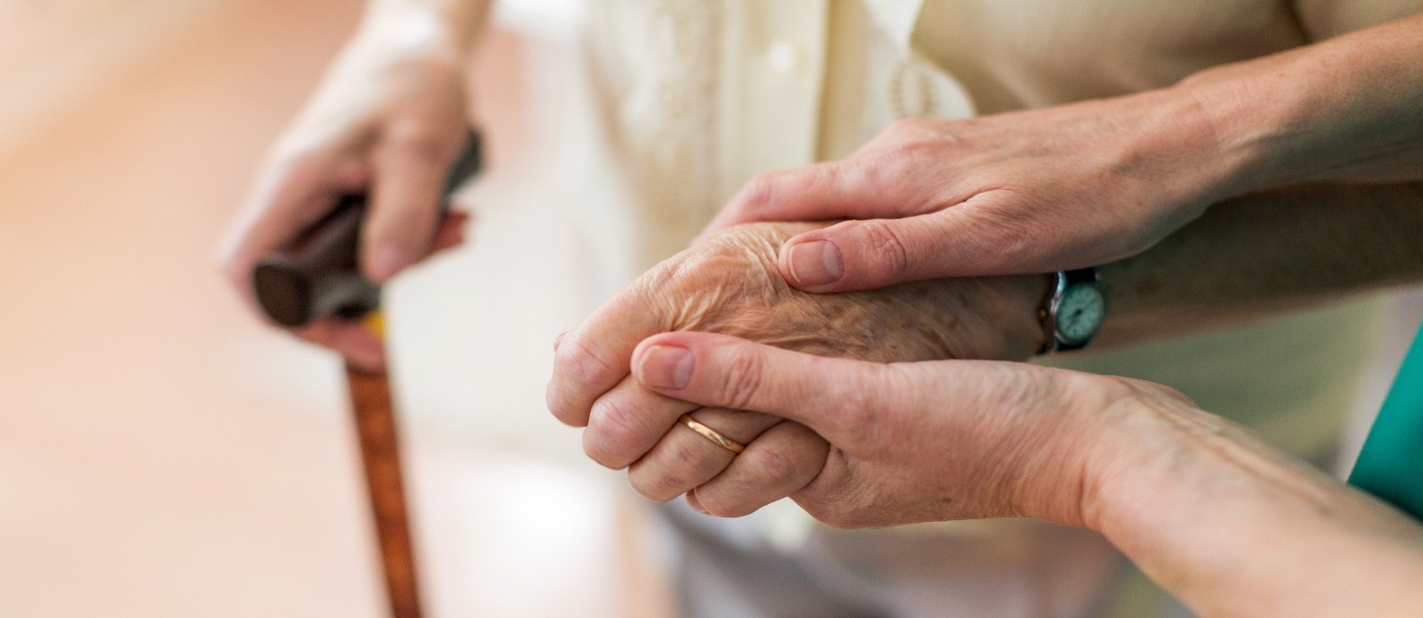 Person holding hands with elderly person who is using a walking stick