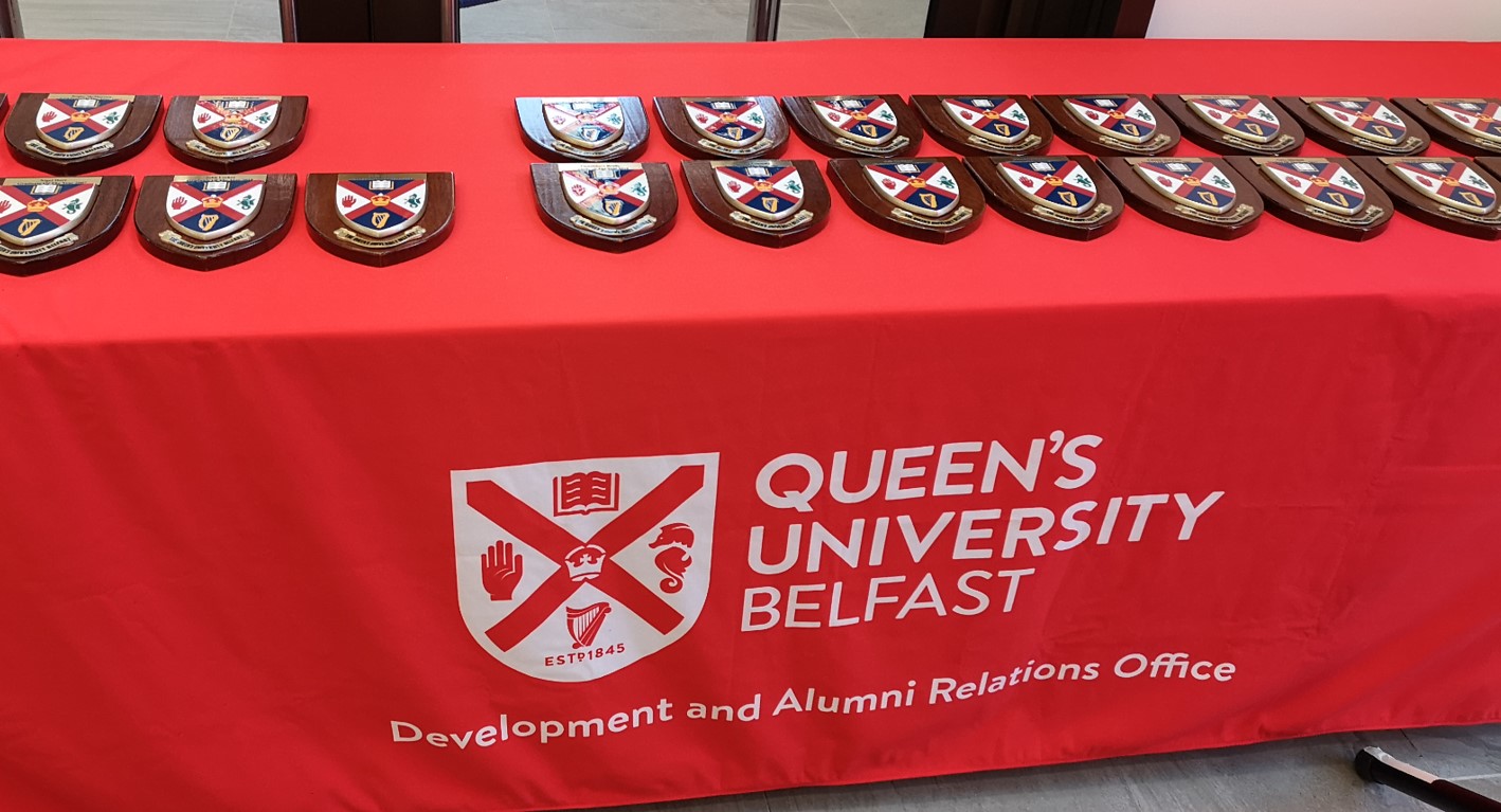 Multiple plaques of Queen's University Belfast crest on a University branded red tablecloth