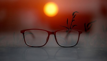 Pair of reading glasses on table with sun setting in background