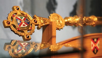 Ornate gold mace, inset with crest of University, sitting on stand at Whitla Hall graduation ceremony