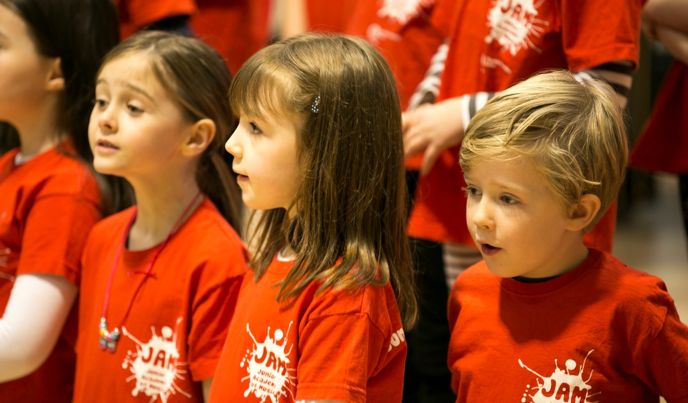 Children listen intently to instructions from their music teacher and sing in a group