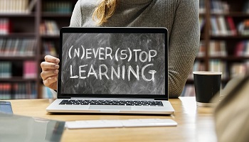 Girl (with library shelves in background) holding open laptop on which the words Never Stop learning appear