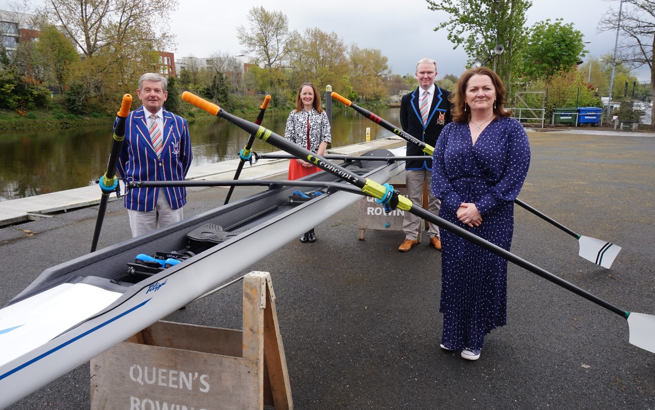 Four people, two men and two women, standing beside a rowing boat by the river