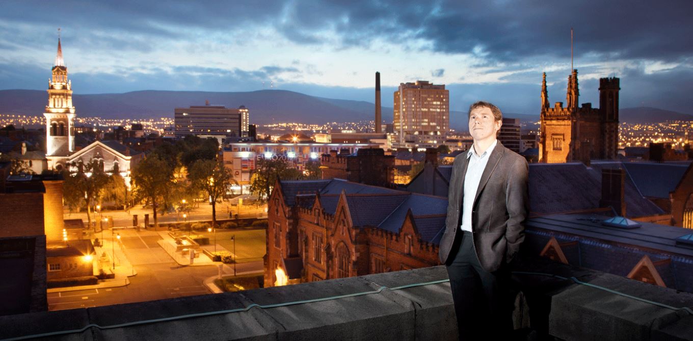 Professor Stephen Smartt looking skyward on roof overlooking University and Belfast skyline at night
