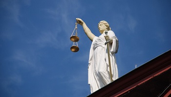 Justice, blindfolded, with scales in one hand and sword in other against blue sky background