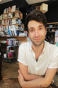 Tom Western wearing white short sleeved shirt with book shelve in the background